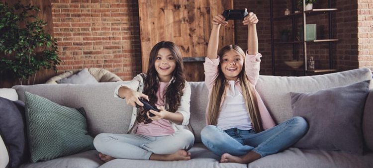 A two kids sitting on sofa and hold video game remotes